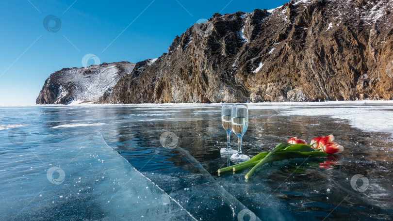 Скачать Два бокала с шампанским и яркими тюльпанами на голубом блестящем льду замерзшего озера фотосток Ozero