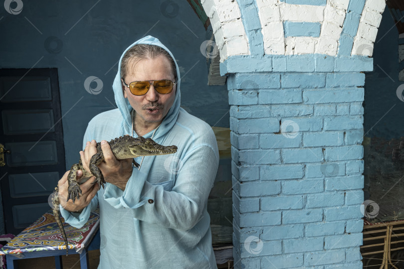 Скачать Мужчина держит в руках маленького крокодильчика и улыбается. фотосток Ozero