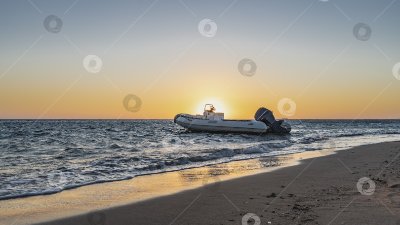 Скачать Рассвет на Красном море. Солнце светит из-за моторной лодки, покачивающейся на волнах прибоя. фотосток Ozero