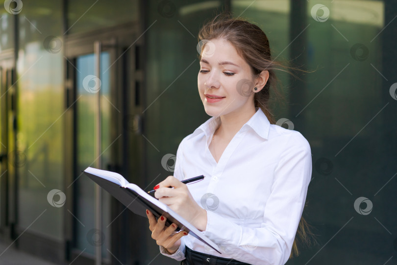 Скачать Успешная красивая деловая женщина, стоящая на фоне зданий, пишет фотосток Ozero