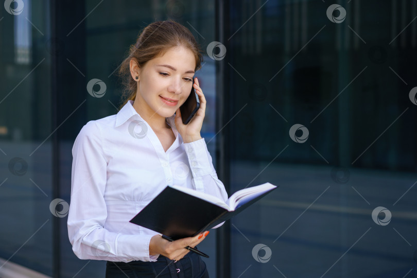 Скачать Молодая деловая женщина разговаривает по телефону и пишет в блокноте фотосток Ozero