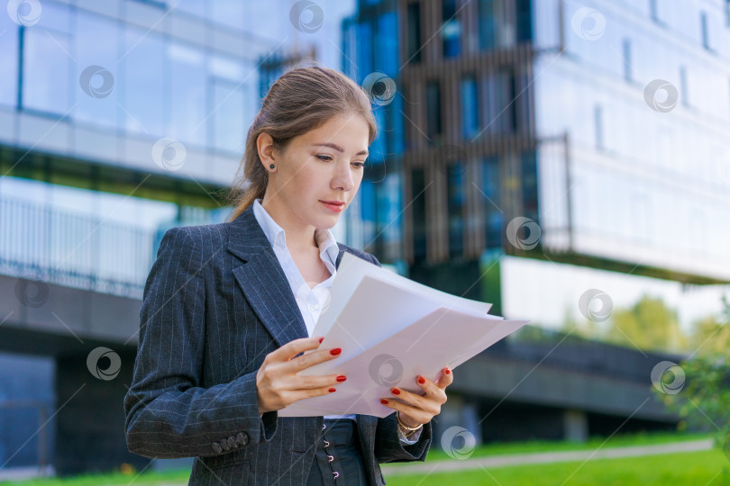 Скачать Молодая деловая женщина с бумагами в деловой одежде на городской улице на фоне фотосток Ozero