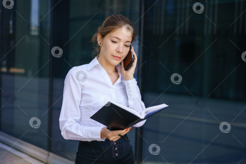 Скачать Молодая деловая женщина разговаривает по телефону и пишет в блокноте фотосток Ozero
