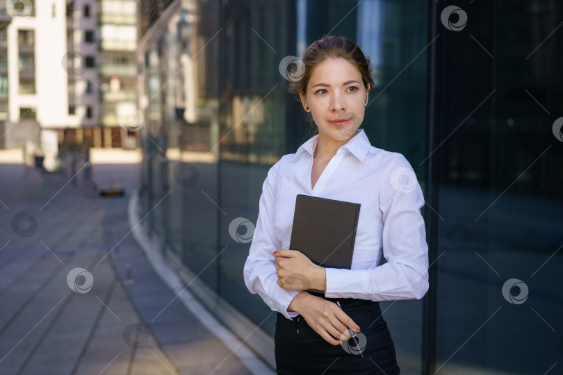 Скачать Молодая деловая женщина с блокнотом в руке возле офисного здания фотосток Ozero