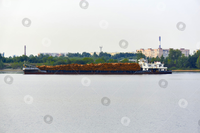 Скачать речной лесовоз, груженный бревнами, движется мимо городского фотосток Ozero