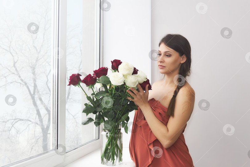 Скачать беременная женщина стоит у окна рядом с букетом роз. фотосток Ozero