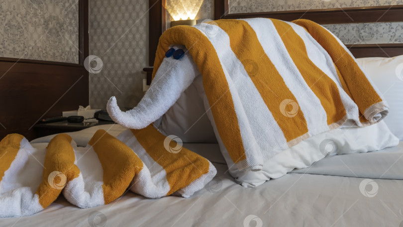 Скачать Декоративный слон, сделанный из подушек и полосатых полотенец, стоит на застеленной кровати в отеле. фотосток Ozero
