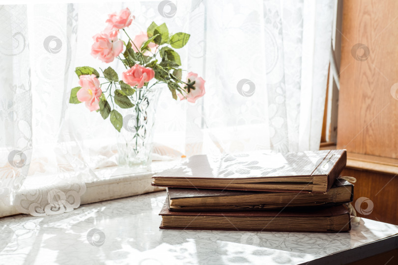 Скачать старинные коричневые фотоальбомы стопкой стоят на столе у окна, а на подоконнике - цветы фотосток Ozero