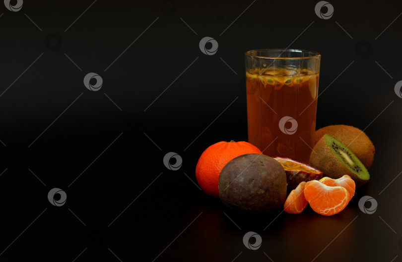 Скачать Стакан свежевыжатого фруктового сока с косточками на черном фоне, рядом с кусочками спелого киви, мандарина и маракуйи. фотосток Ozero
