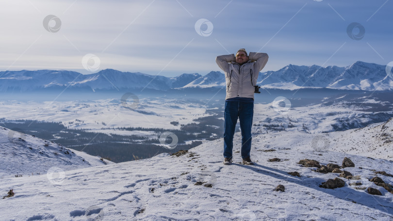 Скачать Мужчина в пуховике стоит на краю заснеженного плато. фотосток Ozero