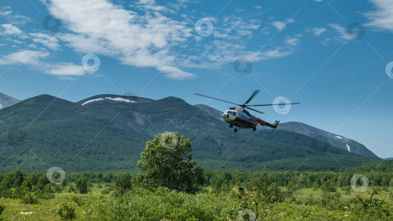 Скачать Туристический вертолет заходит на посадку на зеленом лугу. фотосток Ozero