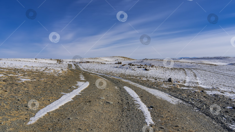 Скачать Грунтовая дорога петляет по заснеженной холмистой долине. фотосток Ozero