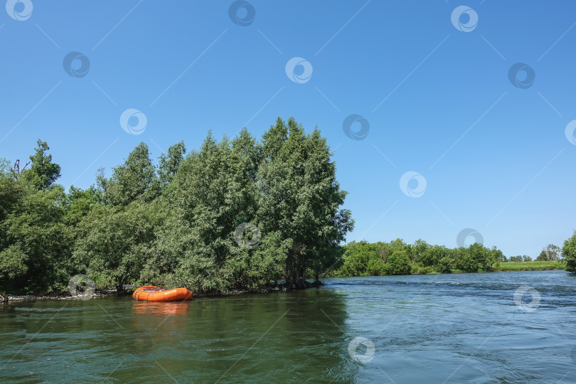 Скачать К берегу реки пришвартована ярко-оранжевая надувная лодка. фотосток Ozero