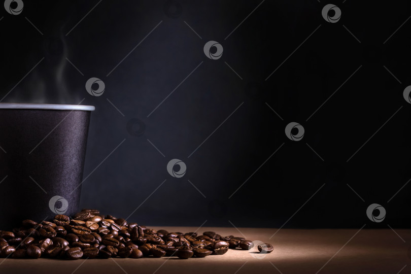Скачать Черная одноразовая чашка кофе с дымом и рассыпанными кофейными зернами на темном фоне фотосток Ozero
