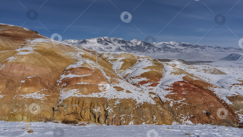 Скачать Ярко-оранжевые холмы и заснеженный горный хребет на фоне голубого неба. фотосток Ozero