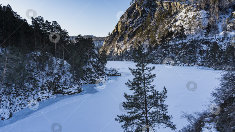 Скачать Замерзшая и покрытая снегом река изгибается между скалами. фотосток Ozero
