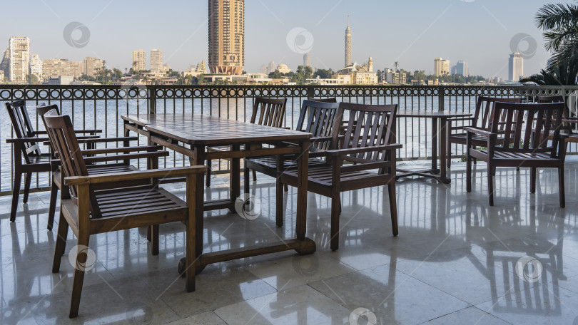 Скачать Деревянные столы и стулья стоят на открытой террасе на берегу Нила. фотосток Ozero