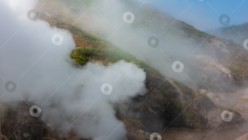 Скачать Облака пара из извергающегося гейзера окутывают склоны холмов. фотосток Ozero