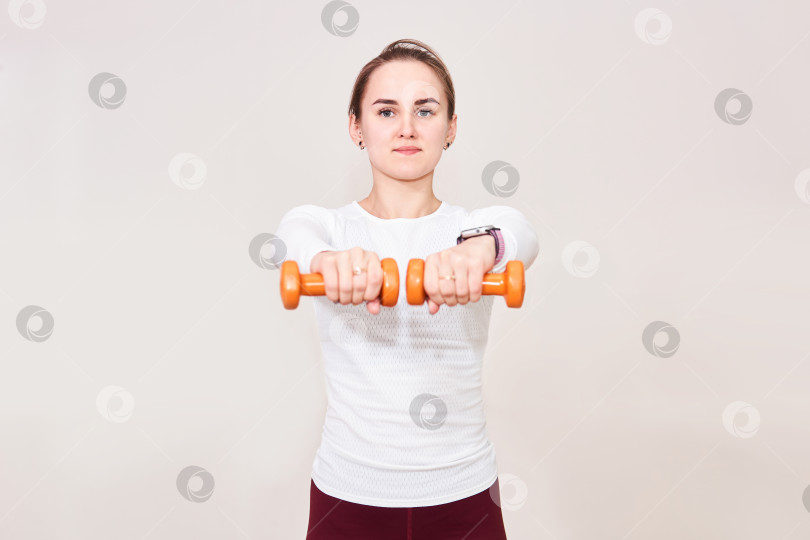 Скачать молодая женщина выполняет упражнения с гантелями, держа их в вытянутых руках. фотосток Ozero