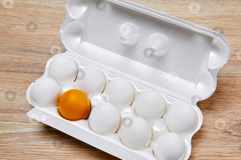 Скачать ящик для яиц с девятью белыми яйцами и одним золотисто-желтым на деревянной подставке фотосток Ozero