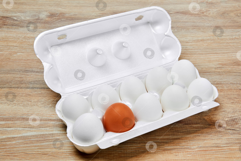 Скачать ящик для яиц с девятью белыми яйцами и одним коричневым, выделенными на белом фоне. фотосток Ozero