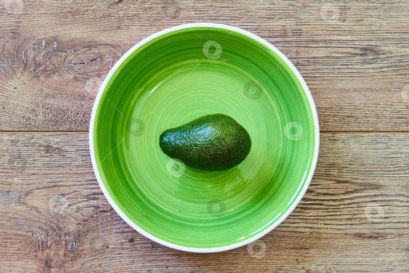 Скачать зеленый авокадо на зеленой тарелке на деревянной столешнице фотосток Ozero