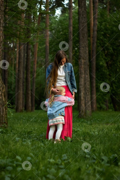 Скачать счастливая девочка-ребенок обнимает свою маму, стоя на траве в парке фотосток Ozero