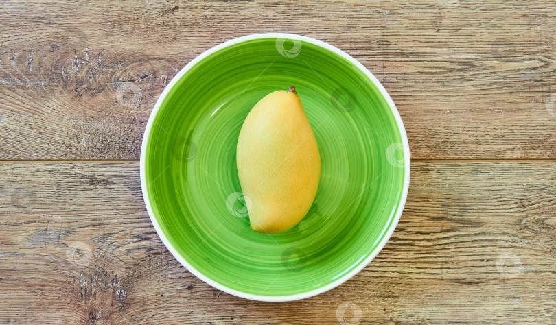 Скачать бледно-желтое манго на зеленой тарелке на деревянной столешнице фотосток Ozero