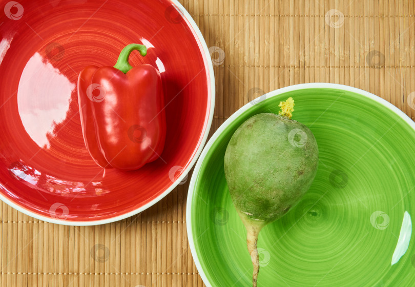 Скачать большая зеленая редька на зеленой тарелке и красный болгарский перец на красном блюде фотосток Ozero