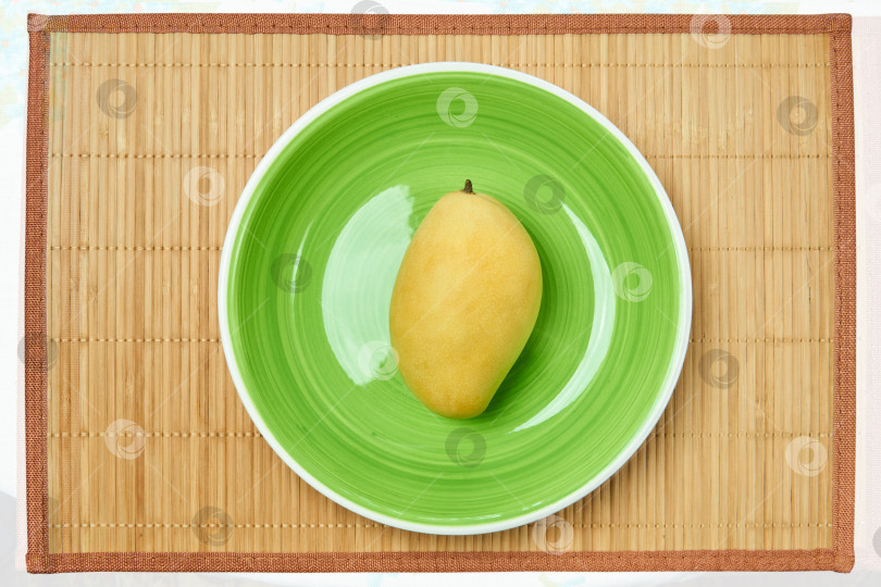 Скачать желтое манго на зеленой тарелке на тростниковом коврике фотосток Ozero
