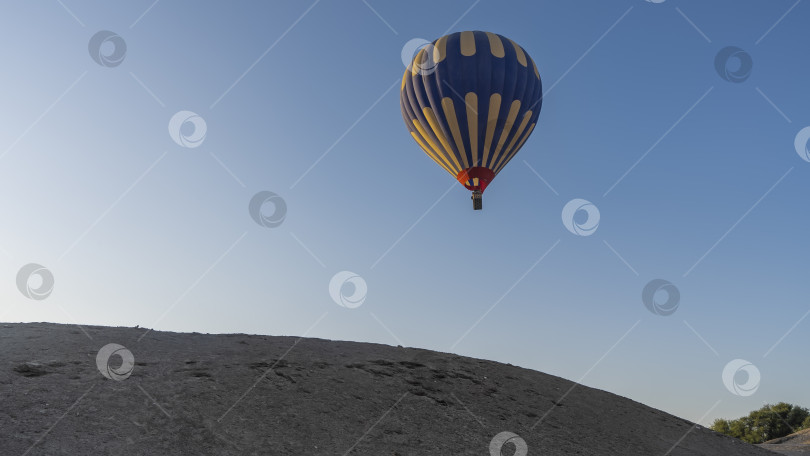 Скачать Яркий желто-голубой воздушный шар летит в ясном лазурном небе над песчаной дюной. фотосток Ozero
