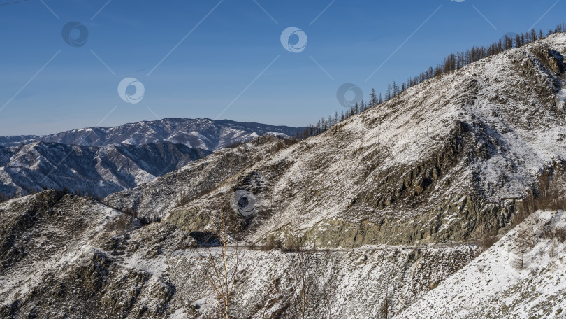 Скачать Дорога проходит по крутому каменистому заснеженному склону горы. фотосток Ozero