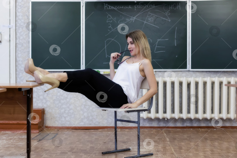 Скачать Строгая молодая учительница-блондинка сидит на стуле, скрестив ноги фотосток Ozero