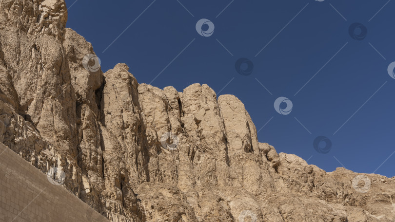 Скачать Живописный утес с крутыми склонами, лишенный растительности, на фоне ясного голубого неба. фотосток Ozero