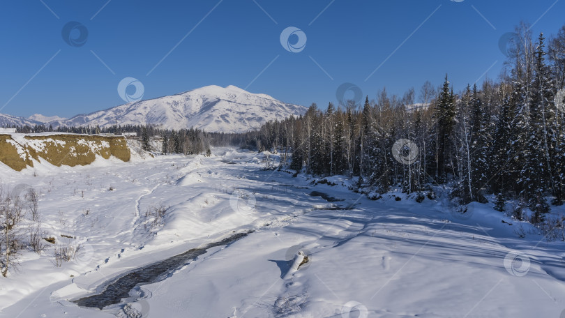 Скачать Замерзшее русло реки покрыто снегом. Лес на берегу. фотосток Ozero