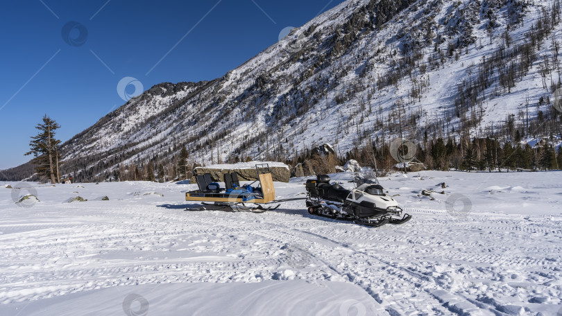 Скачать В заснеженной долине стоит снегоход с прикрепленными к нему санями. фотосток Ozero