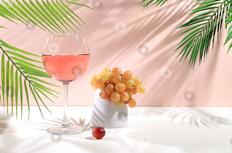Скачать Современный натюрморт с белым вином, алкогольным коктейлем и виноградом на пастельном фоне с длинными резкими тенями, минималистичная концепция для бара, фотосток Ozero