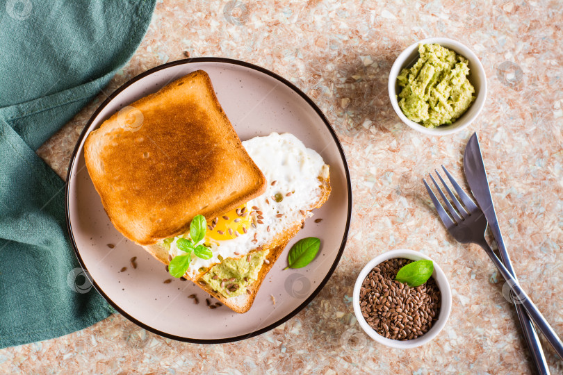 Скачать Сэндвич с авокадо, жареным яйцом и семенами льна на тосте на плите фотосток Ozero