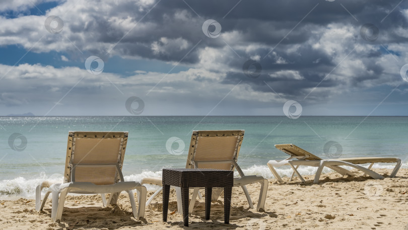 Скачать На песчаном пляже установлены шезлонги и плетеный столик. фотосток Ozero