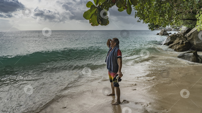 Скачать Мужчина стоит на пляже и смотрит на океан. фотосток Ozero