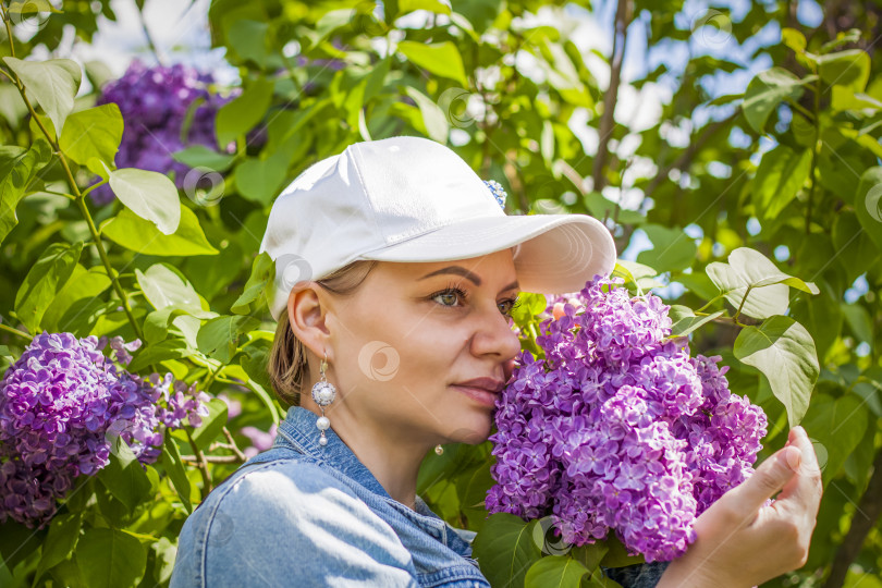 Скачать Молодая женщина в белой шапочке позирует возле куста сирени. Портрет о фотосток Ozero