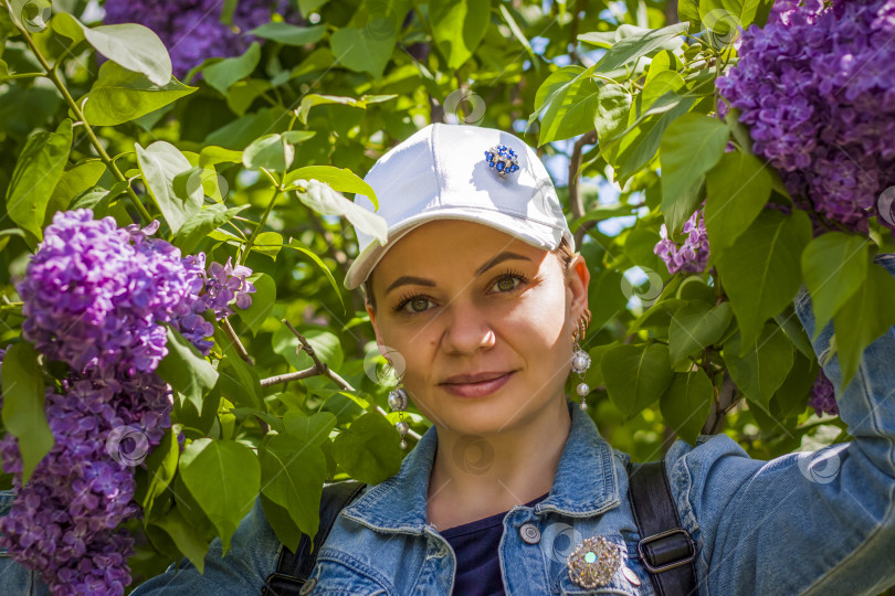 Скачать Молодая женщина в белой шапочке позирует возле куста сирени. Портрет о фотосток Ozero