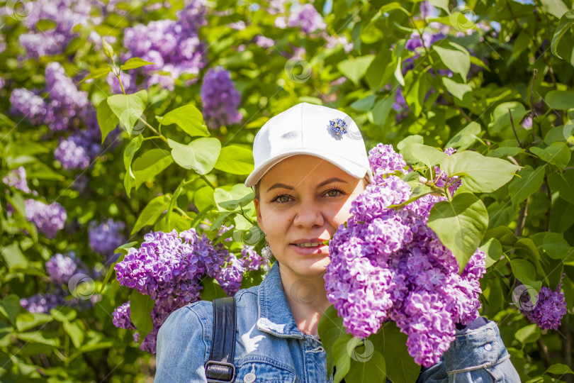 Скачать Молодая женщина в белой шапочке позирует возле куста сирени. Портрет о фотосток Ozero