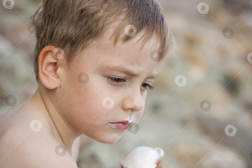 Скачать Симпатичный белокурый мальчик аппетитно ест мороженое летом, сидя фотосток Ozero