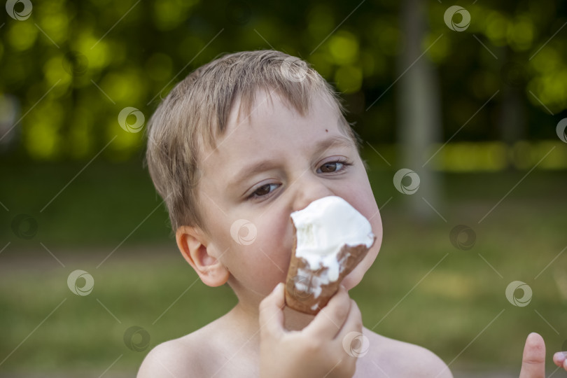 Скачать Симпатичный белокурый мальчик аппетитно ест мороженое летом, сидя фотосток Ozero