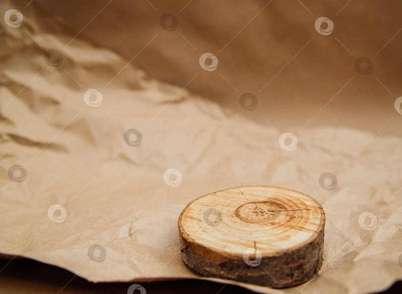 Скачать Круглый кусочек дерева лежит на мятой бежевой крафт-бумаге. Оберточная бумага для посылок и подарков. фотосток Ozero