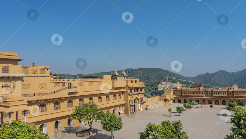 Скачать Янтарный форт в Джайпуре. Вид сверху на площадь, окруженную оранжевыми крепостными стенами с арками и галереями. Горы на фоне голубого неба. Индия фотосток Ozero