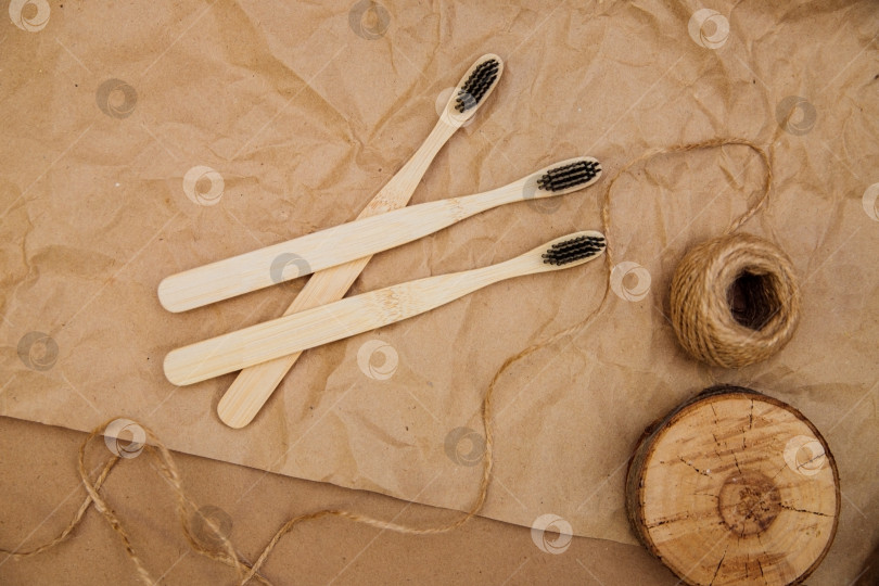 Скачать Три зубные щетки из натурального бамбука лежат на куске дерева на фоне коричневой крафт-бумаги. фотосток Ozero
