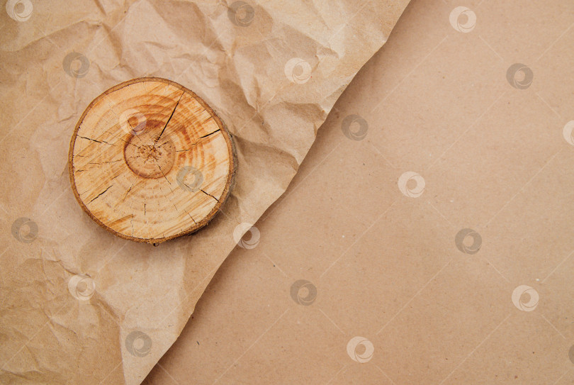 Скачать Круглый кусочек дерева лежит на мятой бежевой крафт-бумаге. Оберточная бумага для посылок и подарков. фотосток Ozero