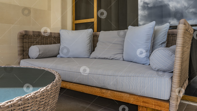 Скачать На террасе стоит плетеный диван с мягкими подушками. фотосток Ozero